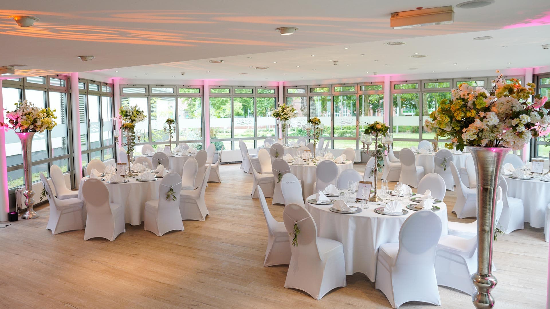 Eleganter Bankettsaal mit weißen Tischdecken und Blumenarrangements, Lichtakzente in Rosa.